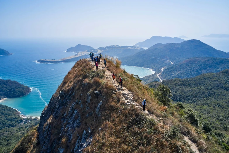 people walk up a steep mountain near the ocean