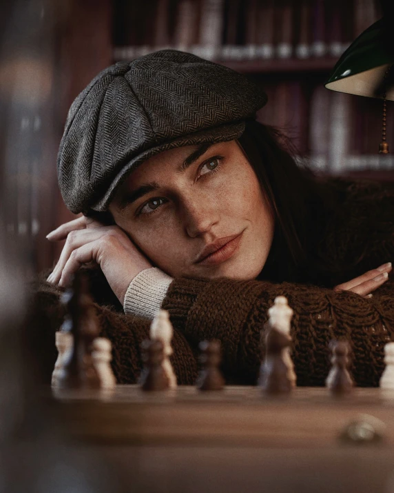 a woman poses with her chin resting on her shoulder with a chess set in front of a liry