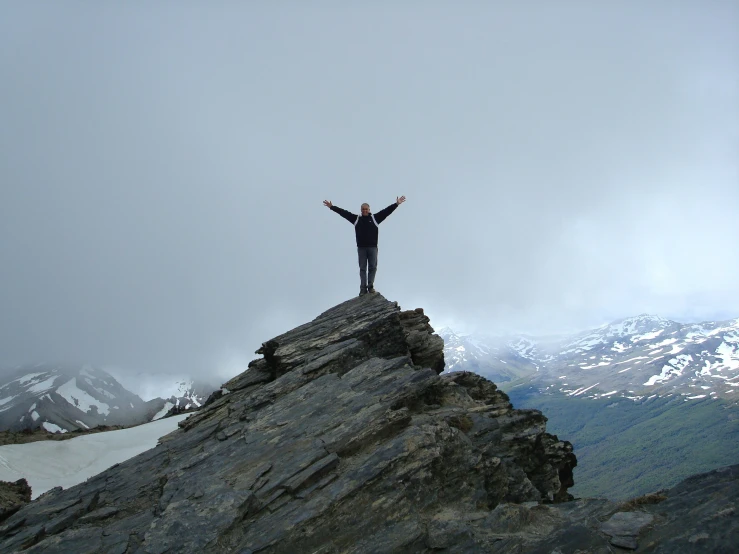 a man standing on top of a tall rock with his hands in the air