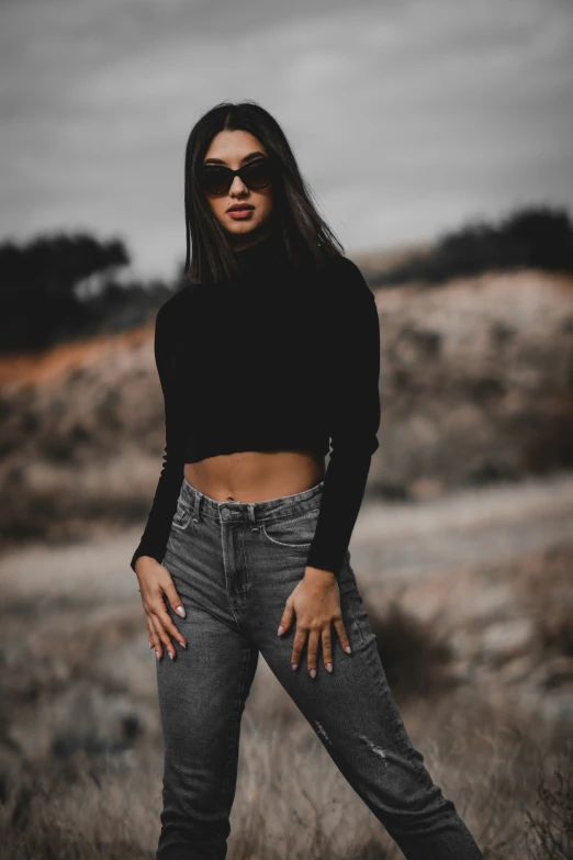 a girl with sunglasses and an off - shoulder crop top standing in the desert