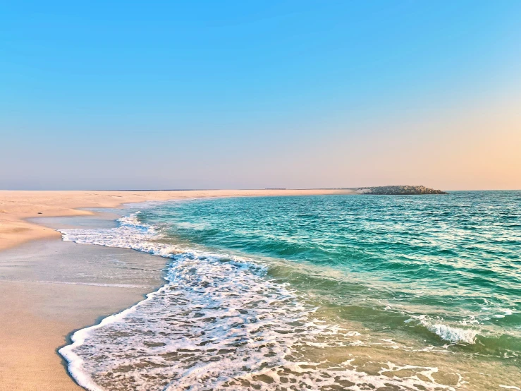 the view of a small island in the ocean from a beach with waves rolling against the shore