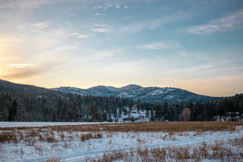 the sun shining on snow covered mountains above a field with brown grass