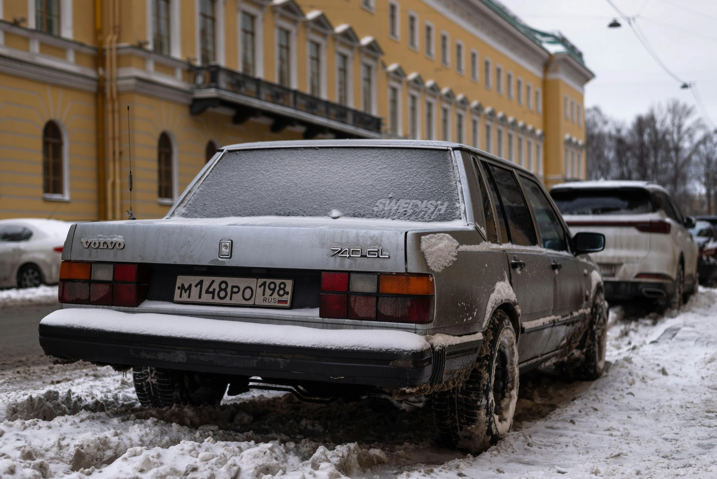 a car with its snow covered taillights sits parked on the side of a city street