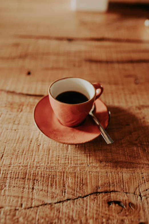 a red coffee cup and saucer are on the wooden table