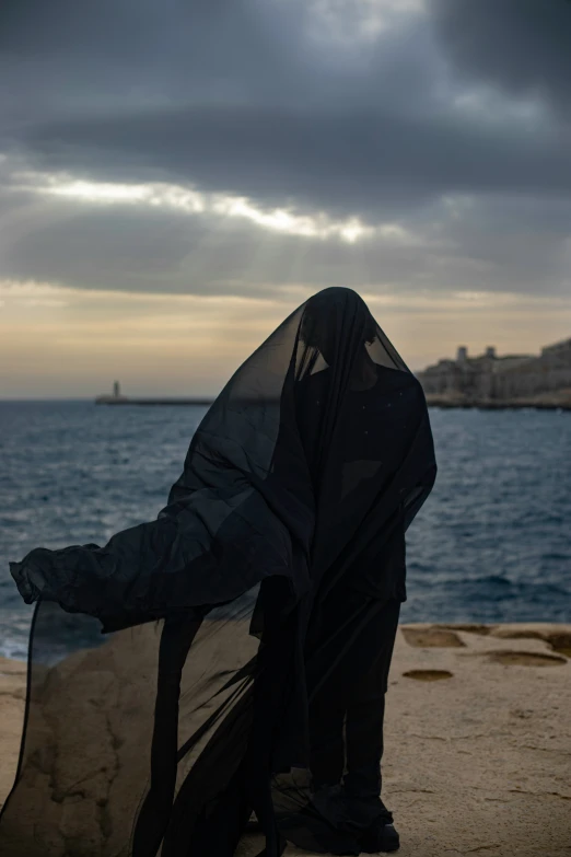 a person in black standing next to the ocean