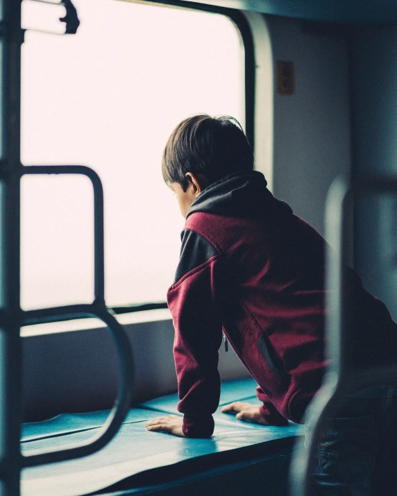 the small child is sitting on a bench looking out the window