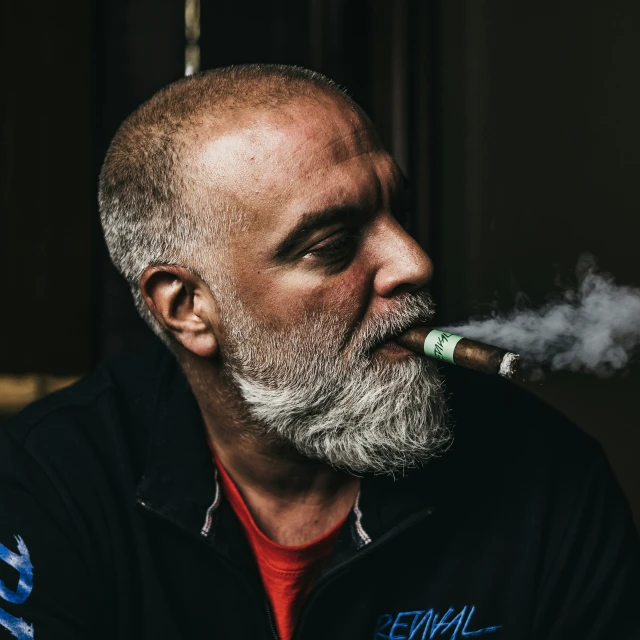 man with gray hair smoking a cigarette wearing a black sweater