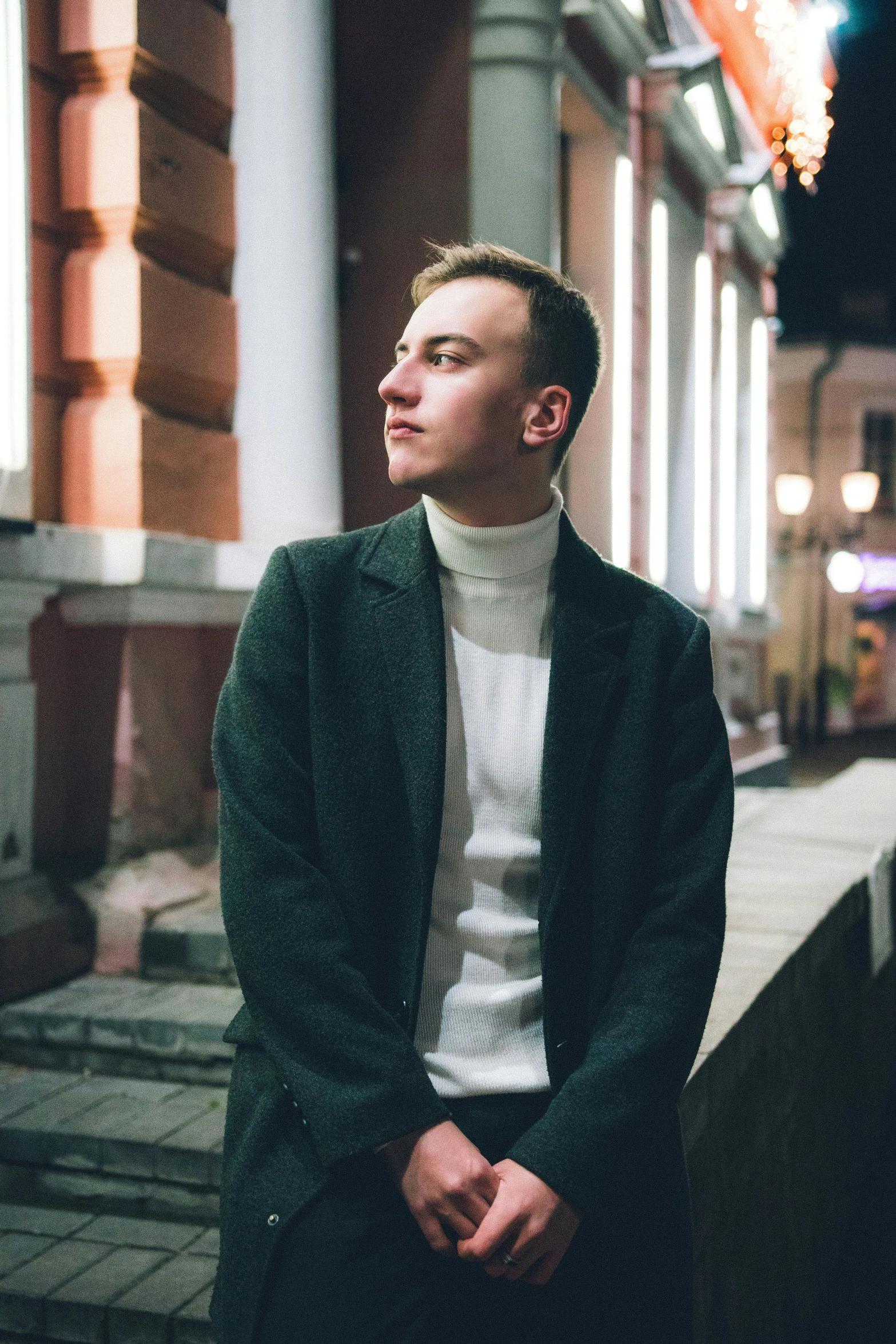 man in green blazer, white sweater and black pants looking away from the camera