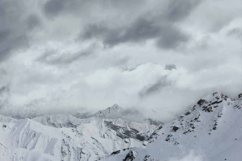 mountain peak covered in snow and snow drifts with clouds over it