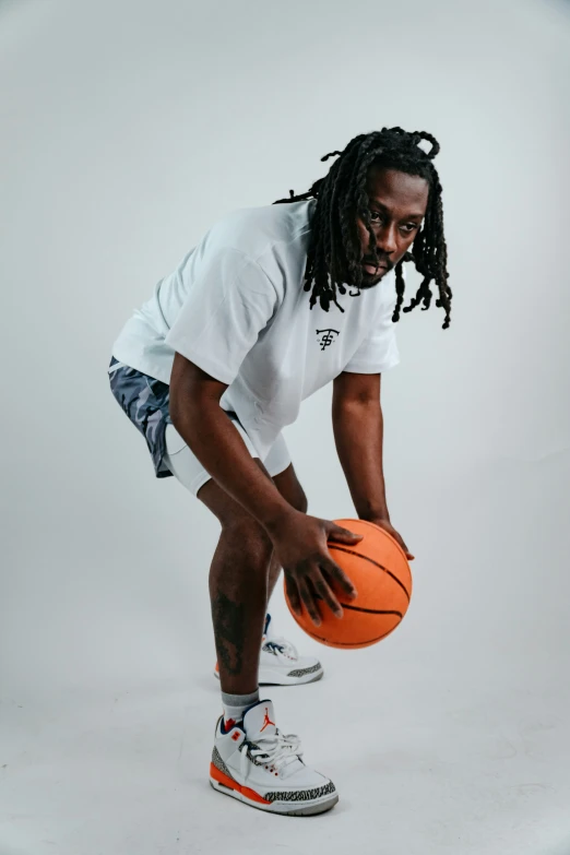 a young black man in a white shirt with dreadlocks holds a basketball