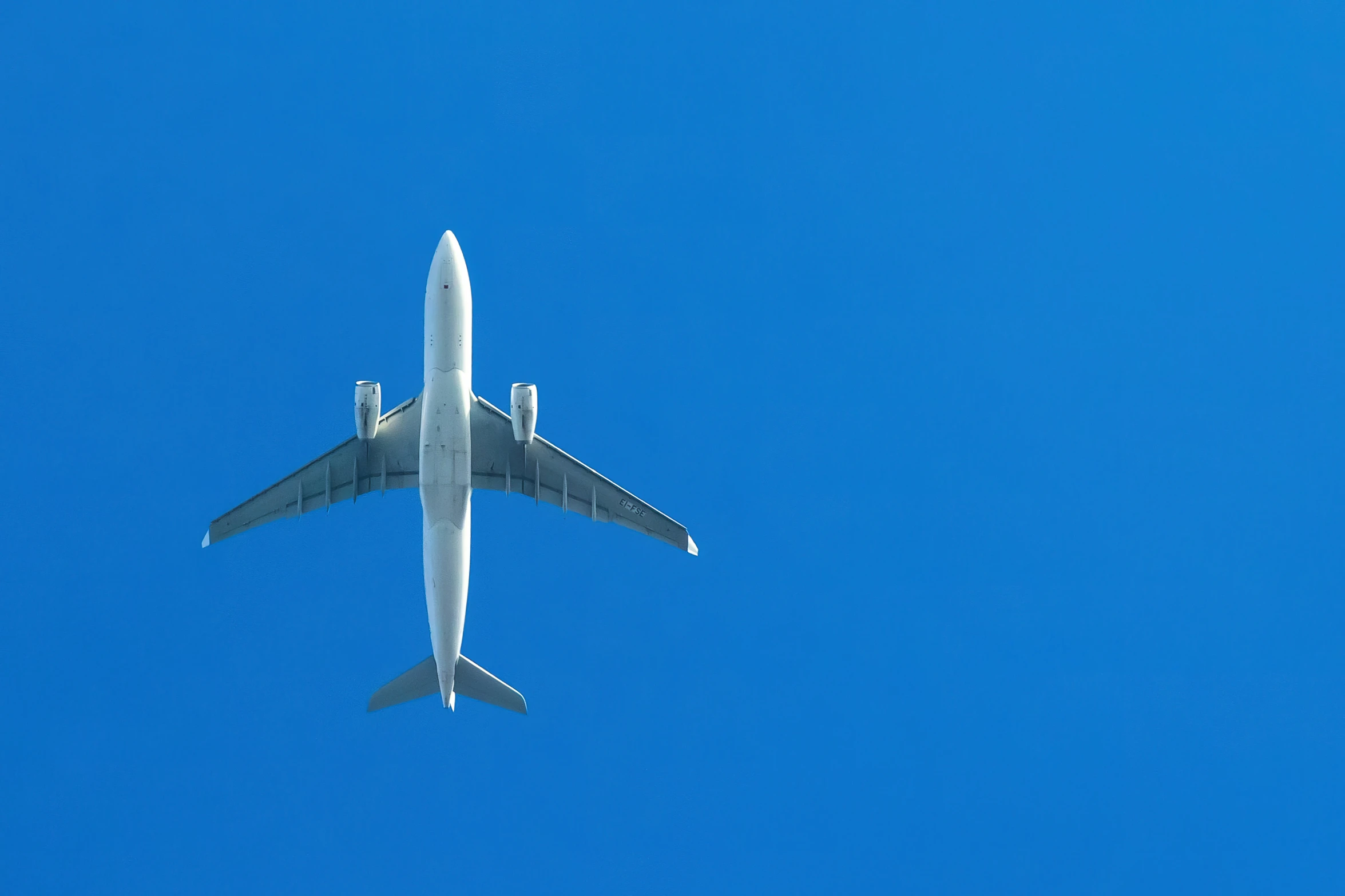 the underside view of a plane flying in a blue sky