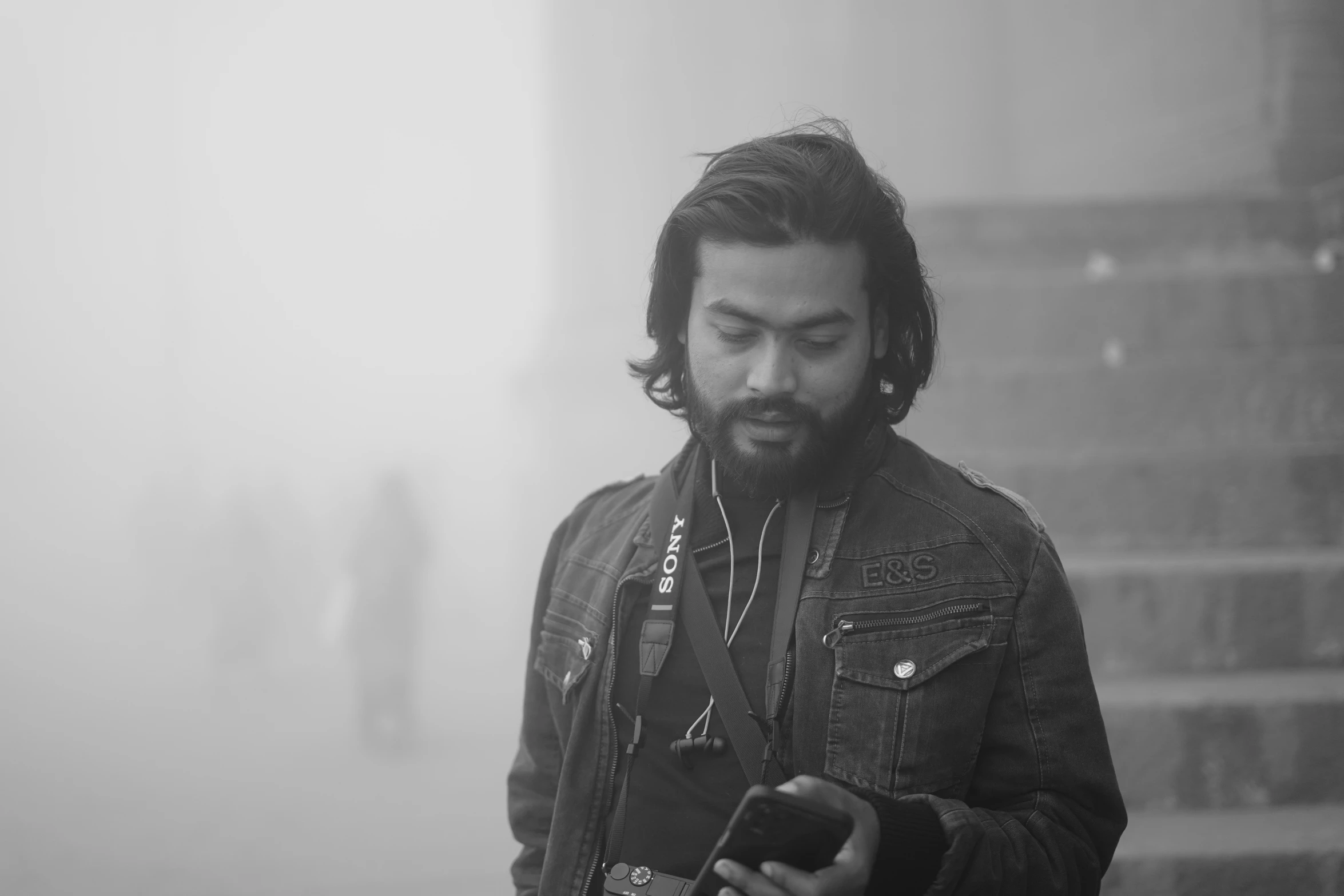 a bearded man using a smart phone in a foggy day