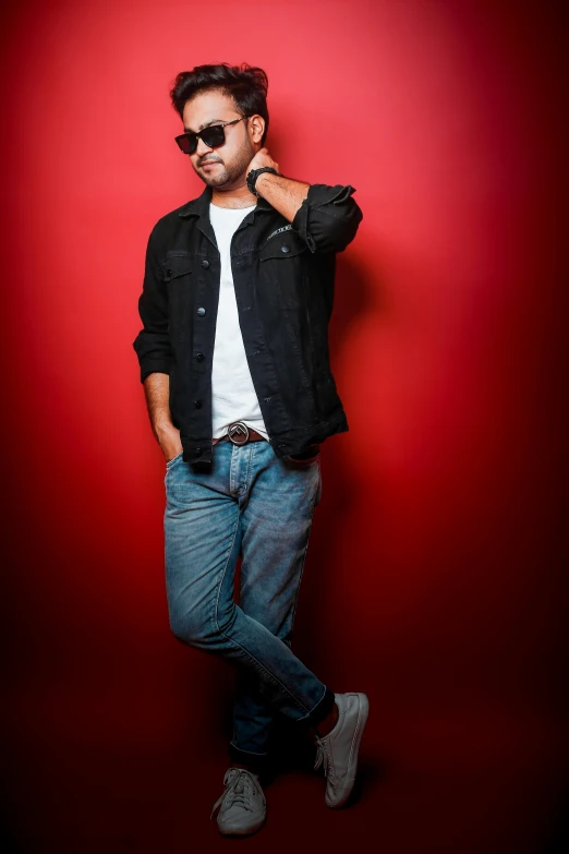 a man in a denim jacket standing on a red wall