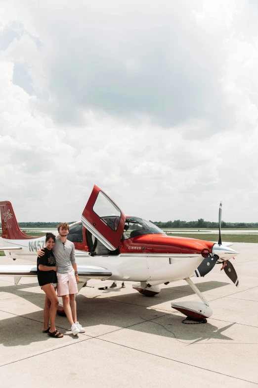 two people pose with a small red and white airplane