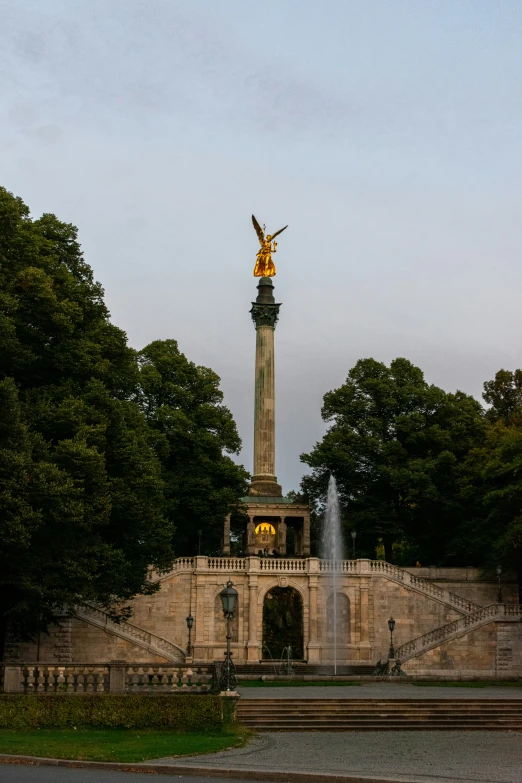 a statue sits in front of the trees near water