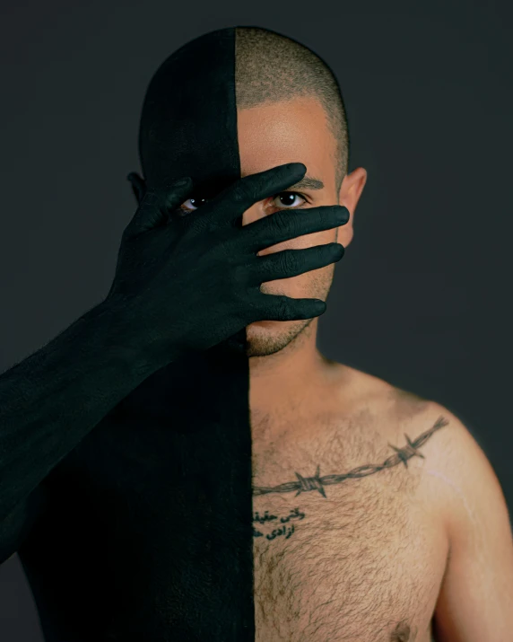 a shirtless male wearing all black holds his hands on the side of his face