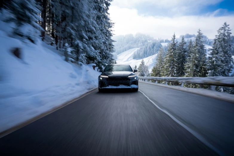 a black car driving down the road next to snow covered mountains