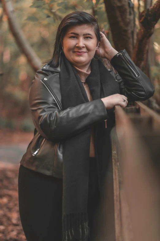 a woman with long hair and a leather jacket leans against a wooden rail