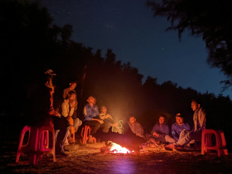 a group of people sitting around a camp fire in the dark