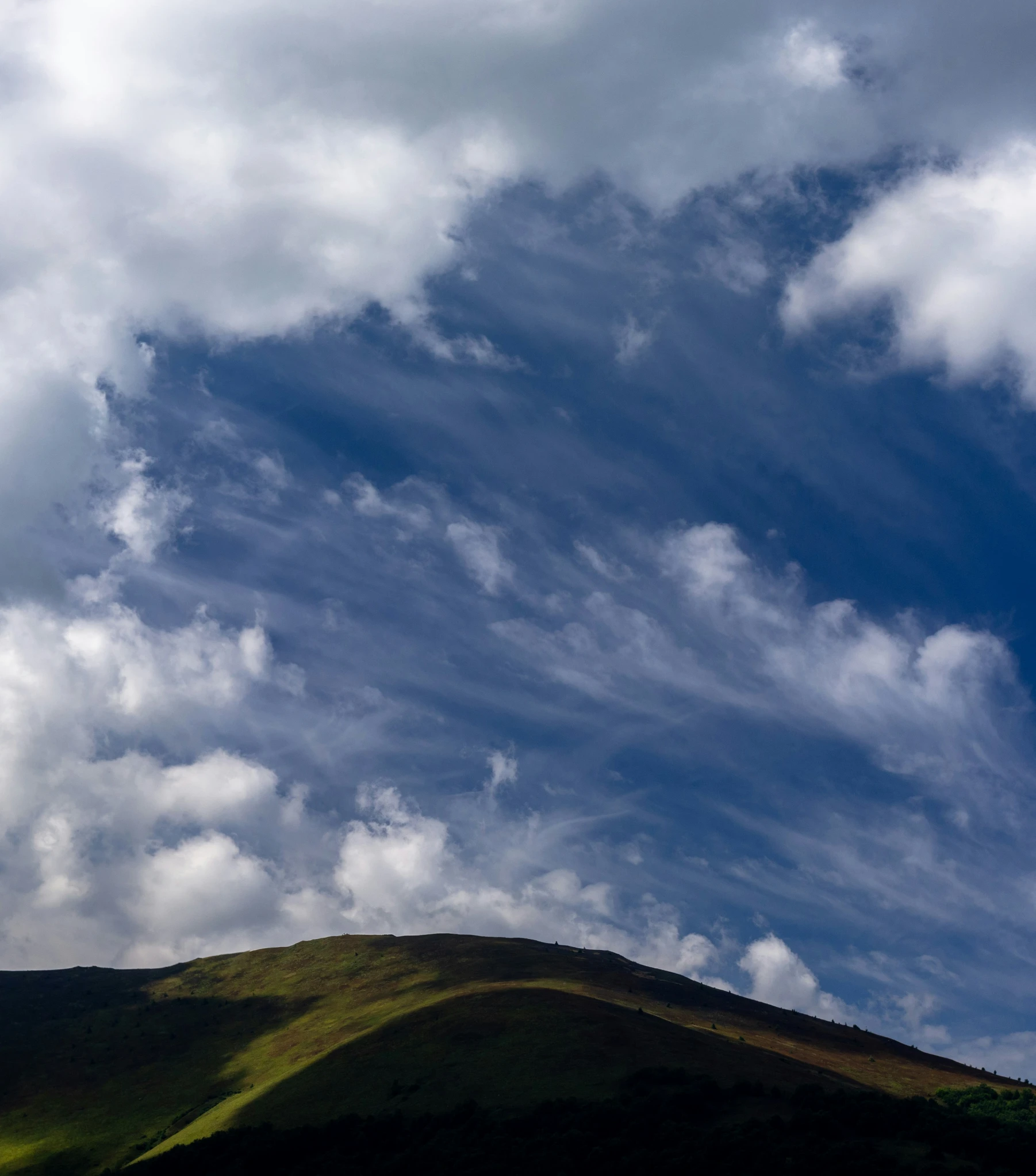 a big grassy hill covered in clouds and blue skies