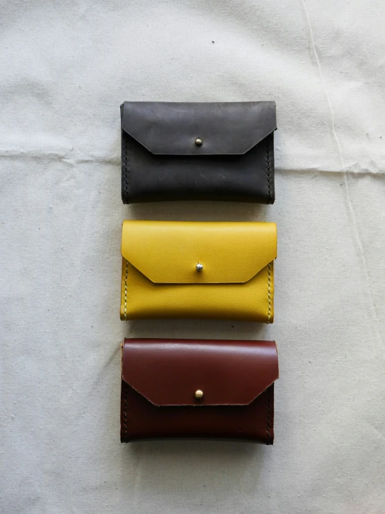three different leather wallets are lined up against the white sheet