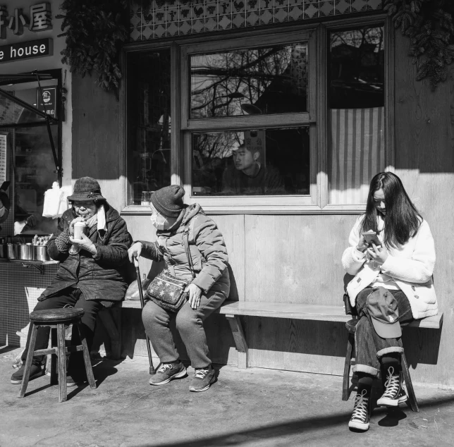 three women sitting outside and one knitting on a bench