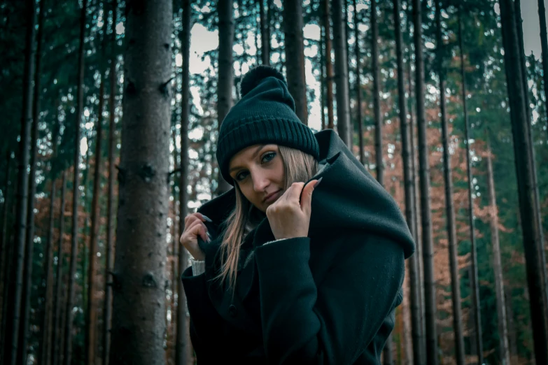 woman in green sweater and hat standing next to tree trunks