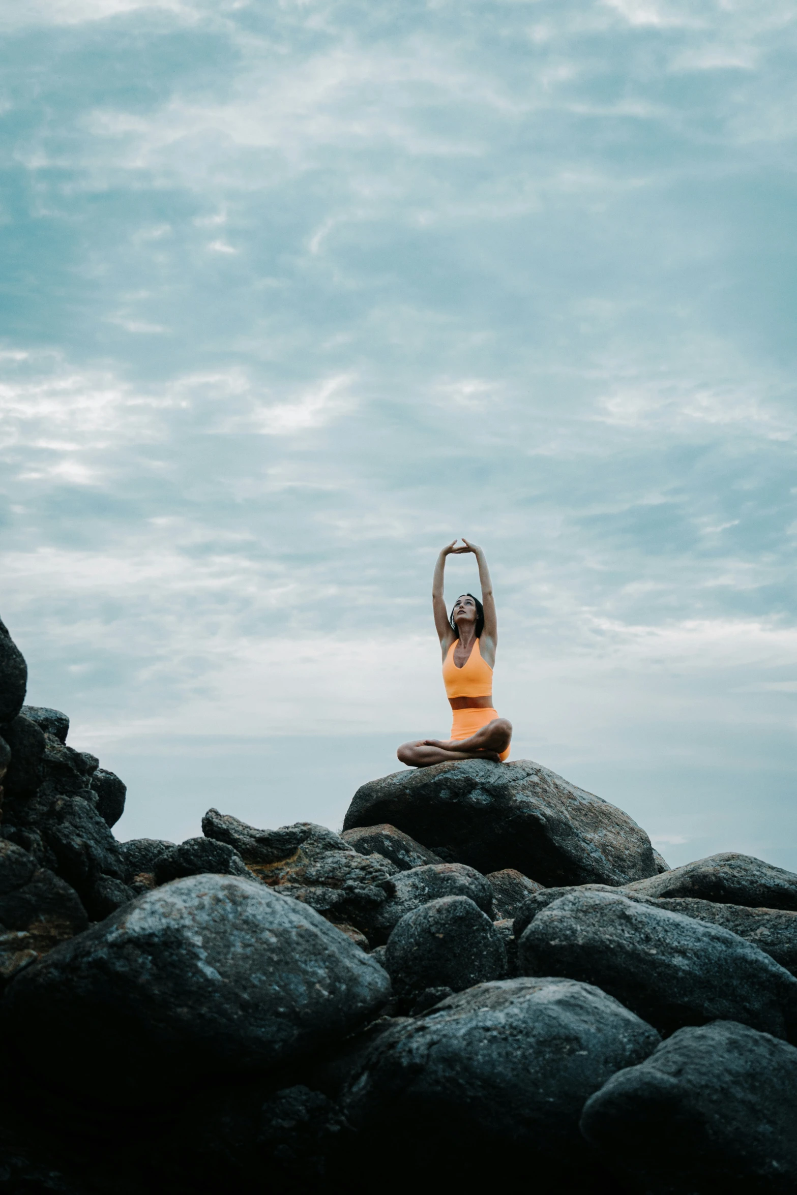 woman meditating sitting on rock with arms above head