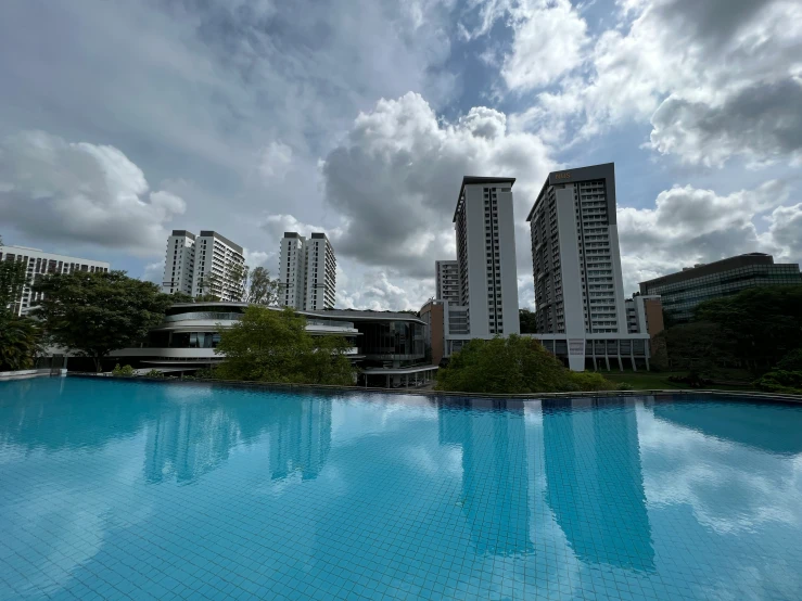 a large swimming pool next to tall buildings under a cloudy sky