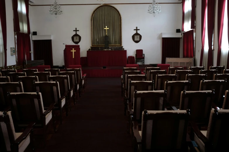 a dimly lit church with red pews and a cross