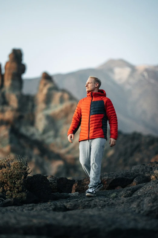 a man in orange jacket standing on rock with mountains in background