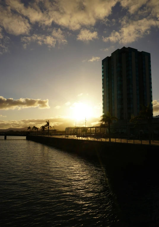 the sun is rising over a tall building next to a body of water