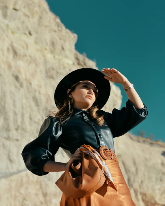 a woman in black hat and dress holding a tan bag