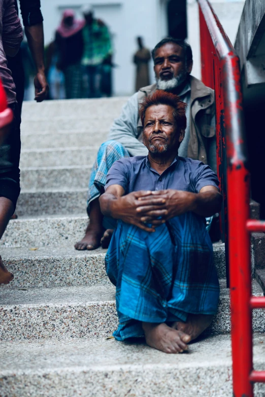 a man sitting on a set of stairs in front of another man with his arms folded