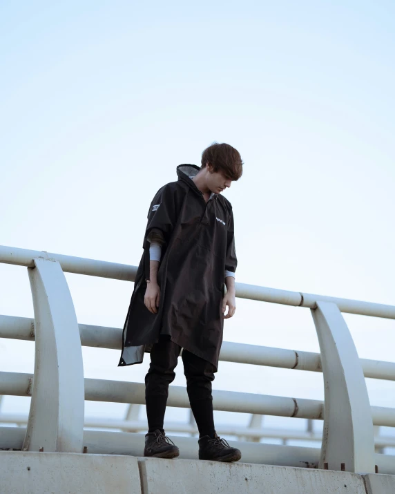 a boy in black jacket standing on bridge rails