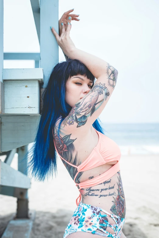 a tattooed woman with blue hair leaning against a metal railing