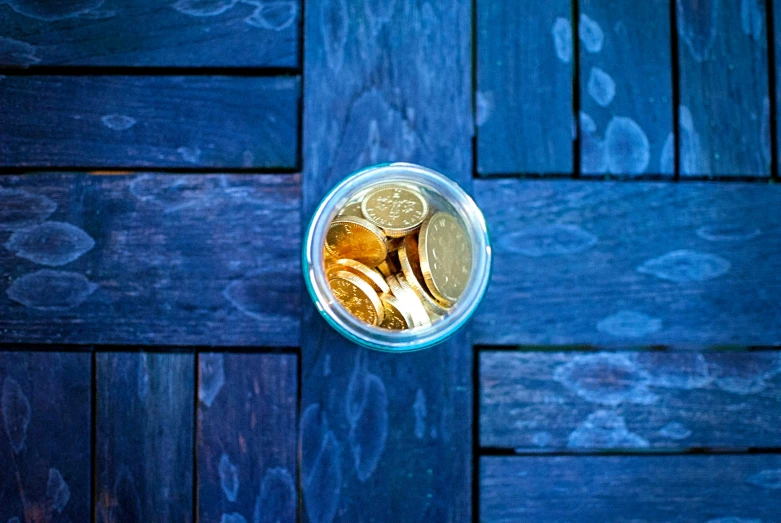 gold coins sitting in a clear jar next to a wooden table