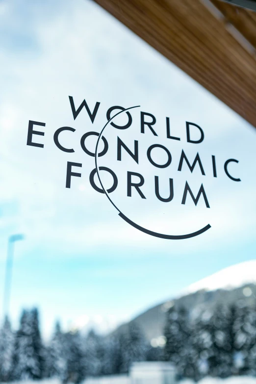 the word'world economic forum'is on the glass in front of a snowy tree - covered mountain