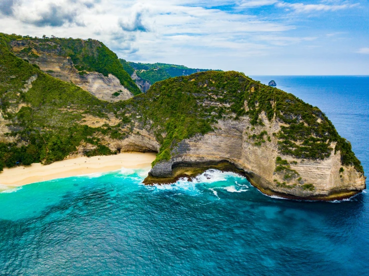 an island surrounded by hills, a sandy beach and clear blue water