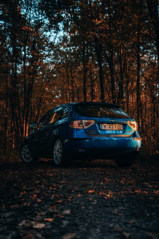 a blue car parked on a gravel road by some trees