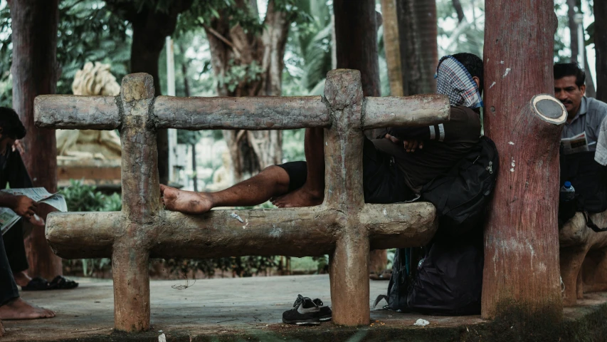 a man sitting on a wooden bench with his legs hanging off a log