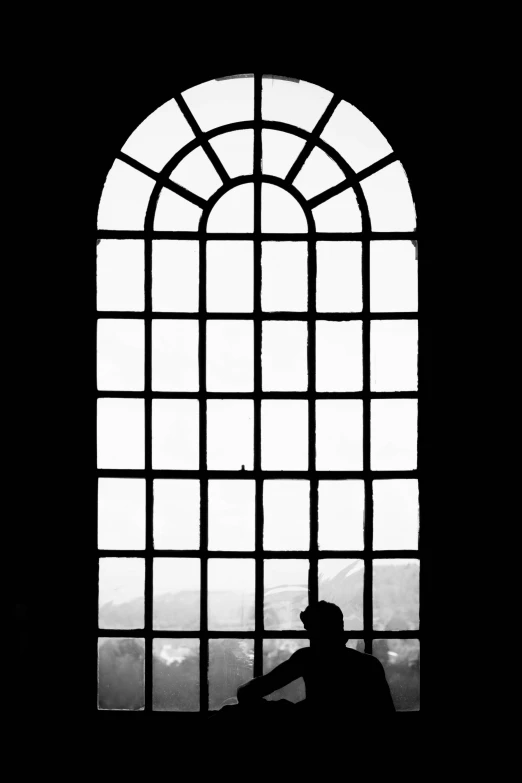 silhouette of a man sitting alone in front of an arched window