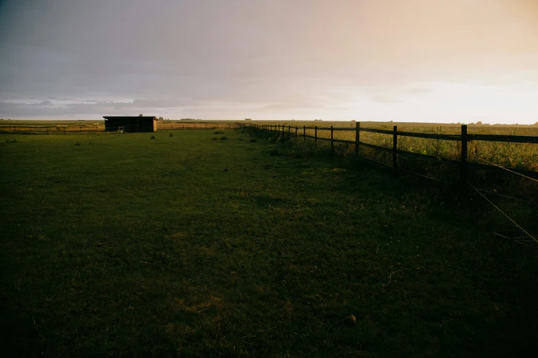 the sun is setting over the grass field behind a fence