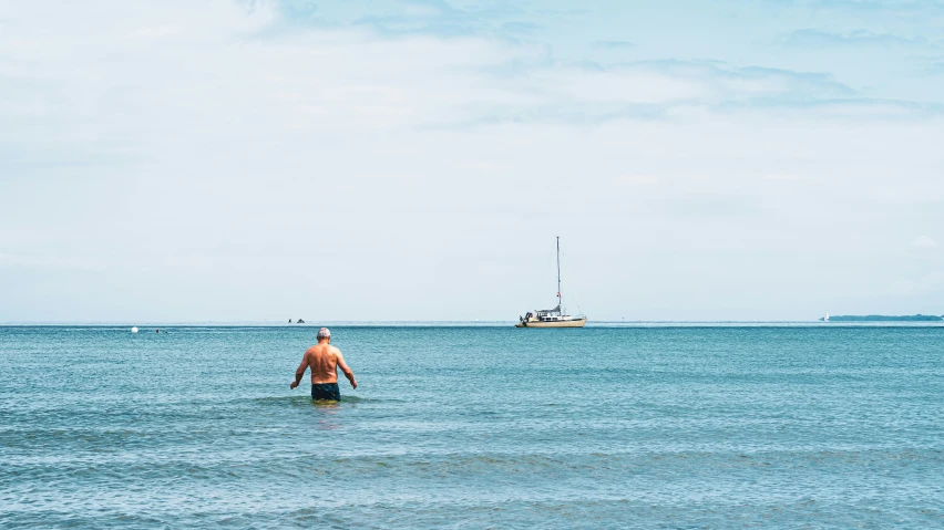 a man wading in the ocean next to a boat