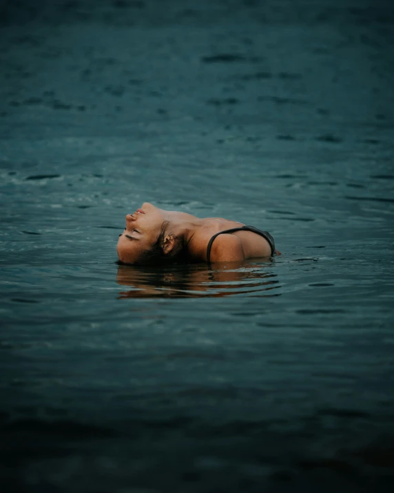 a young woman laying in the water near a pier