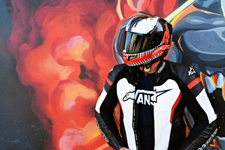 the motorcyclist wears a racing suit and helmet in front of a colorful mural