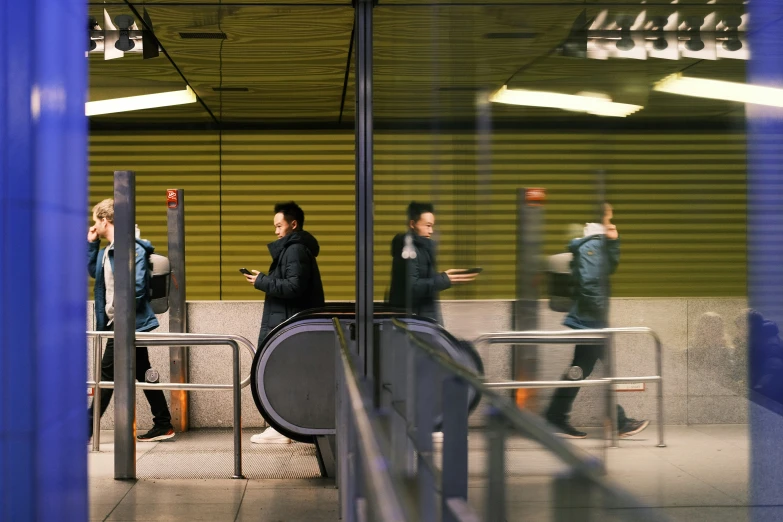 two guys using their cell phones as they wait for the train