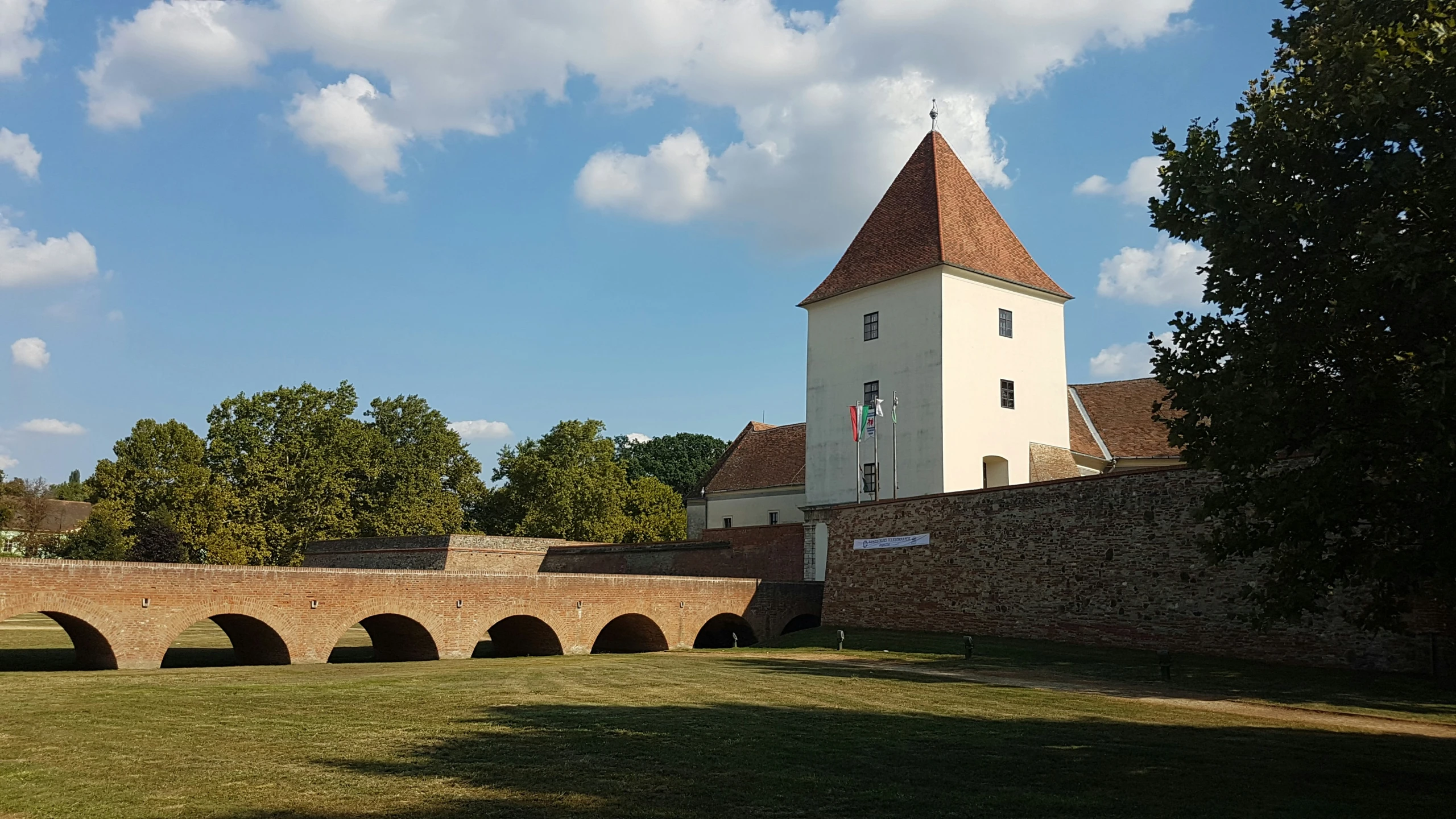 a large tower building near an old brick fence and bridge