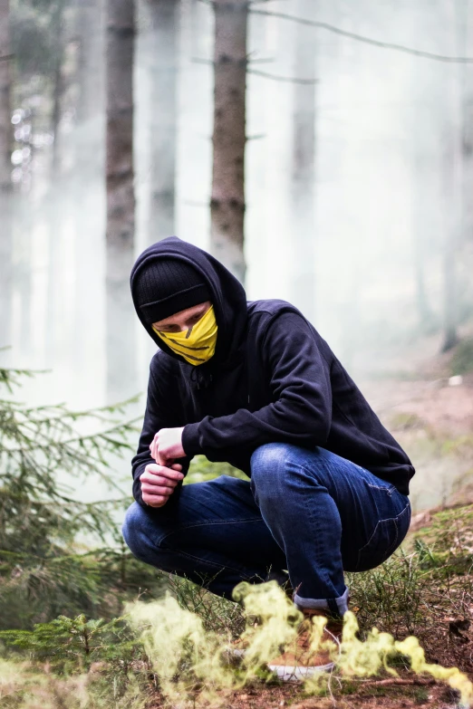 a man with a mask crouches down in the woods