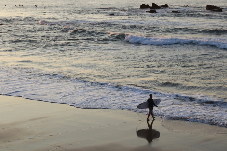 surfer walking into the ocean while holding his board